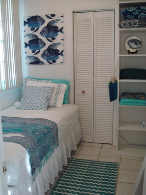 A bedroom with a bed, a wardrobe, a shelf with decorative items, and a patterned rug.