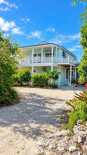 A two-story building with a balcony, surrounded by greenery and a gravel driveway.