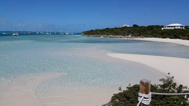 A beach with clear turquoise water, a sandy shore, and a white building in the background. -  PARADISE/ ask discount Sept/Oct- bonefishing, beaches/town/360 view, 98 5 stars (Georgetown)