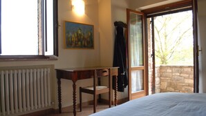 A bedroom with a bed, a desk, a chair, a radiator, a painting, and a window with a view of trees. - 10 minutes walk from Todi center, with pool (Todi)