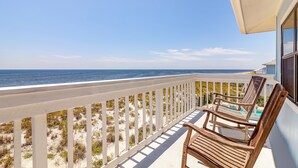 Een balkon met uitzicht op de oceaan, houten stoelen en een zwembad.