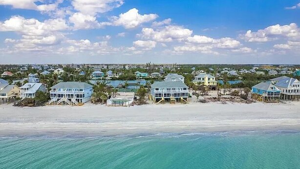 Een kustwoongebied met huizen aan het strand, heldere lucht en turquoise water.