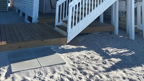 Een tweelaags strandhuis met een houten terras en een trap naar de bovenverdieping.