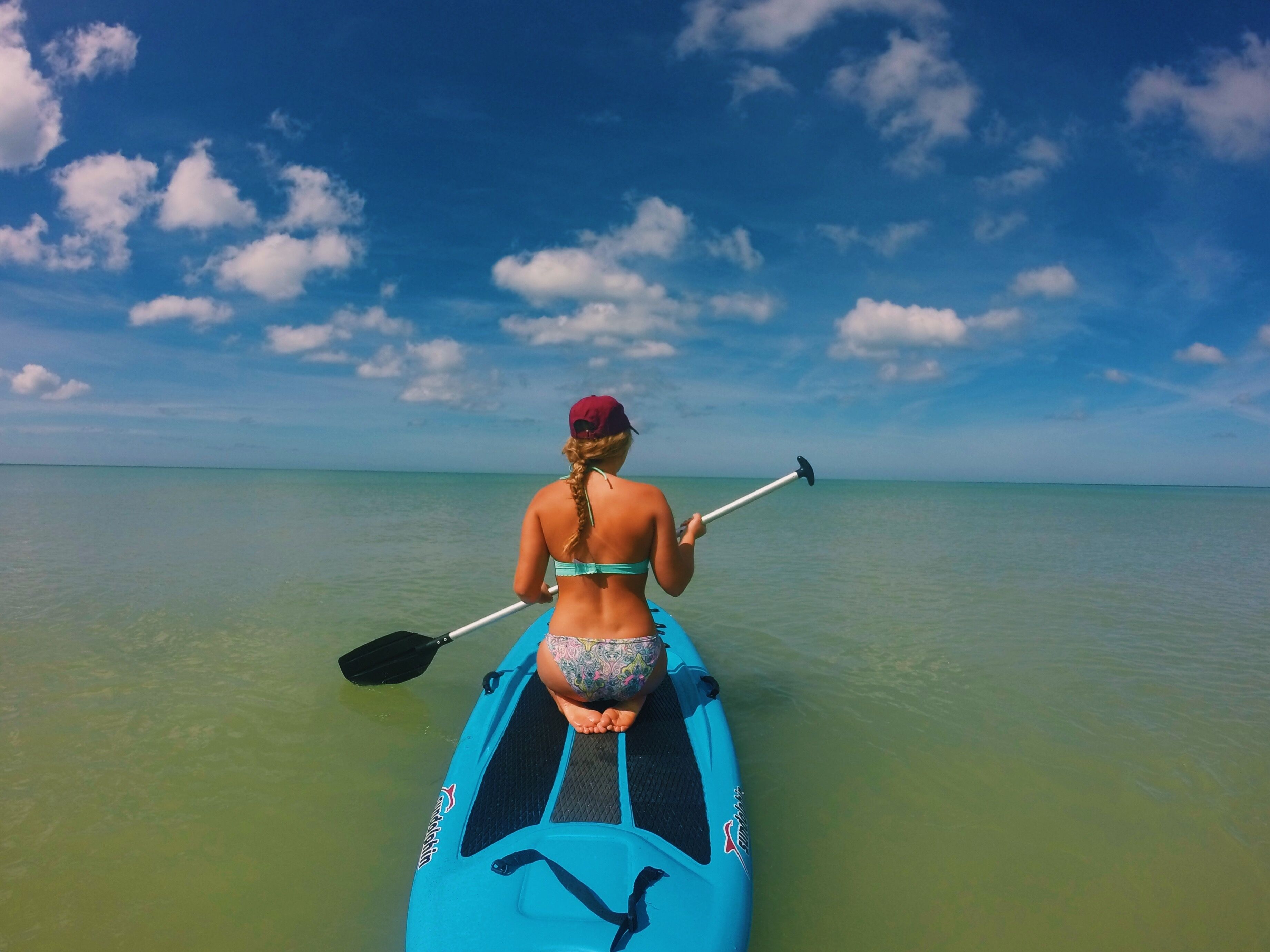 A person on a paddleboard in clear water, with a blue sky and clouds above.