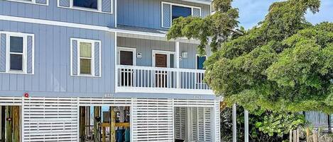 A multi-story building with a balcony, a covered entrance, and a sandy ground.