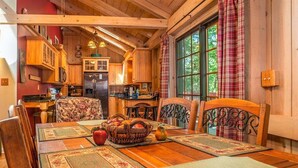 A cozy wooden cabin interior with a dining area, kitchen, and large windows. - Grey Haven Cabin in Connestee Falls (Brevard)