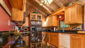 A kitchen with wooden cabinets, a stainless steel refrigerator, a dishwasher, and a dining table with chairs. - Grey Haven Cabin in Connestee Falls (Brevard)