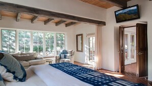 A bedroom with a large bed, a sofa, a chair, and a TV. There are large windows and a door leading outside. - HISTORIC EAST SIDE ~ Warm and inviting Walk to canyon road. (Santa Fe)