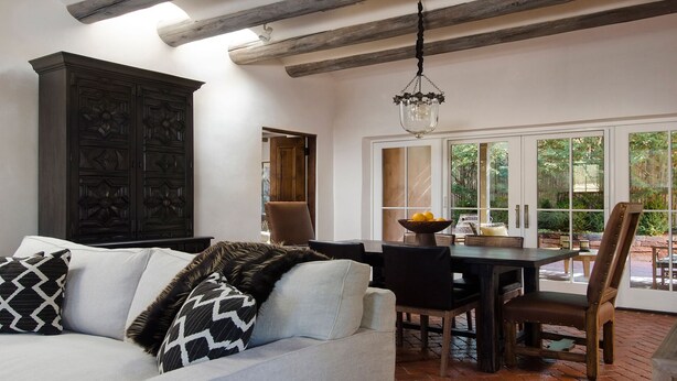 A living room with a sofa, a dining table with chairs, a chandelier, and a large cabinet. - HISTORIC EAST SIDE ~ Warm and inviting Walk to canyon road. (Santa Fe)
