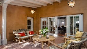A sunlit patio with wicker furniture, a round wooden table, and a vase of flowers. - HISTORIC EAST SIDE ~ Warm and inviting Walk to canyon road. (Santa Fe)
