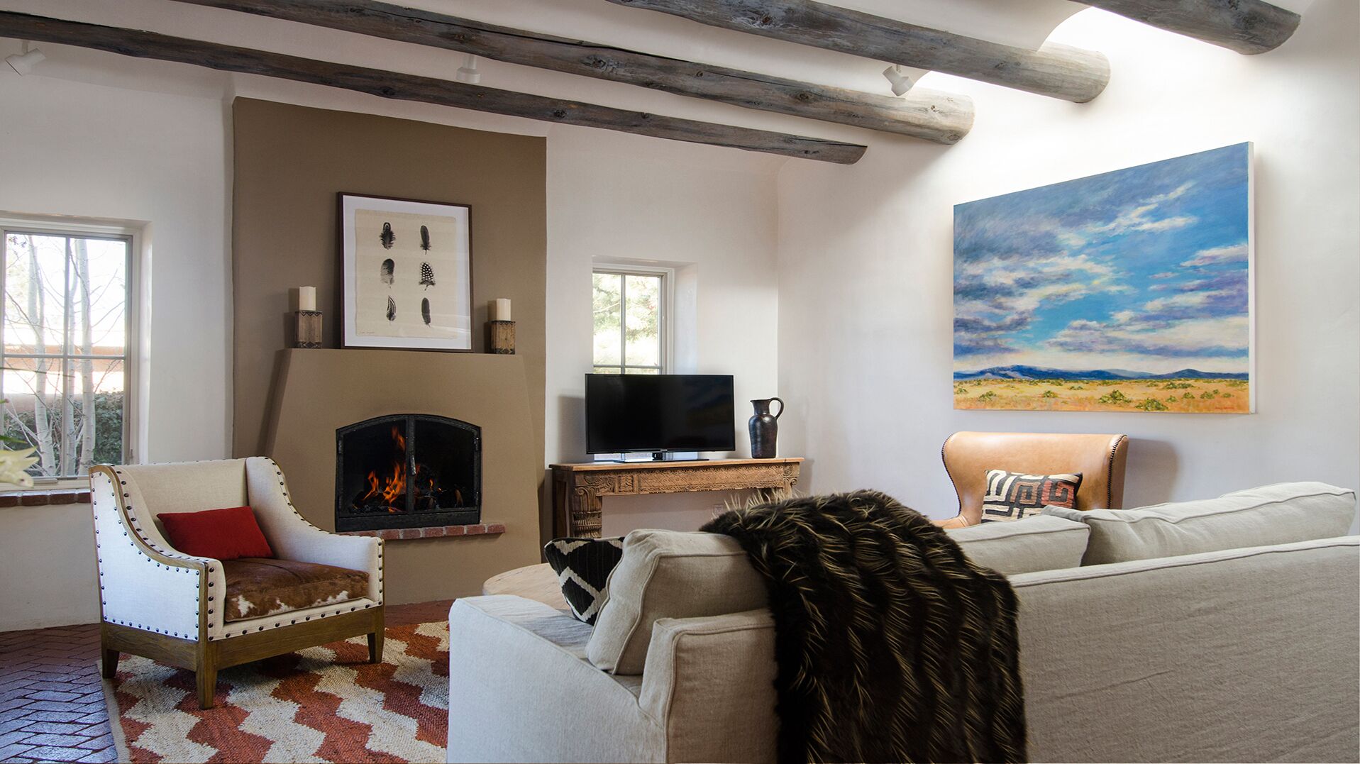 A living room with a fireplace, a television, and a painting of a landscape.