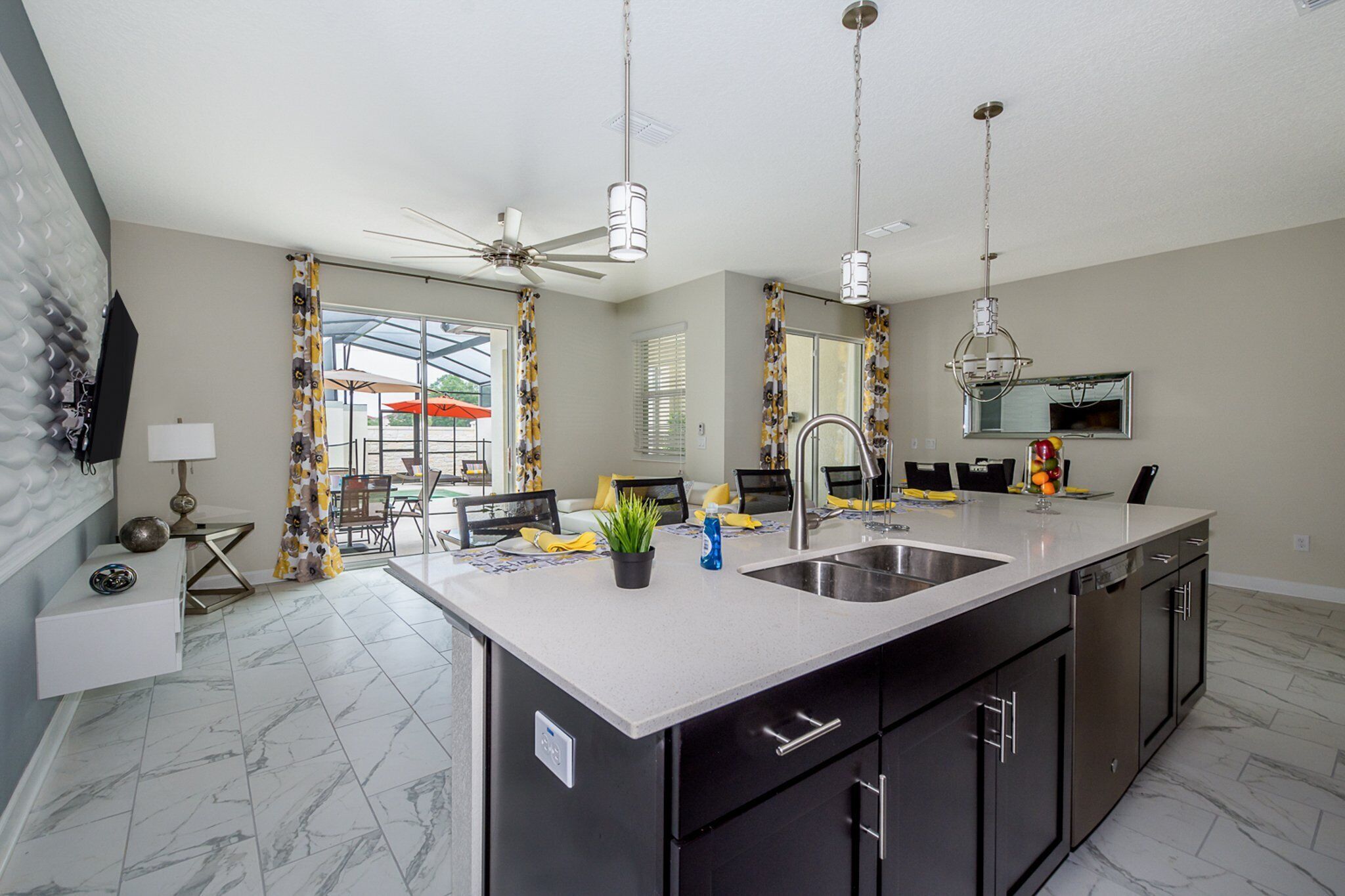 A modern kitchen with a large island, black cabinets, and a ceiling fan.