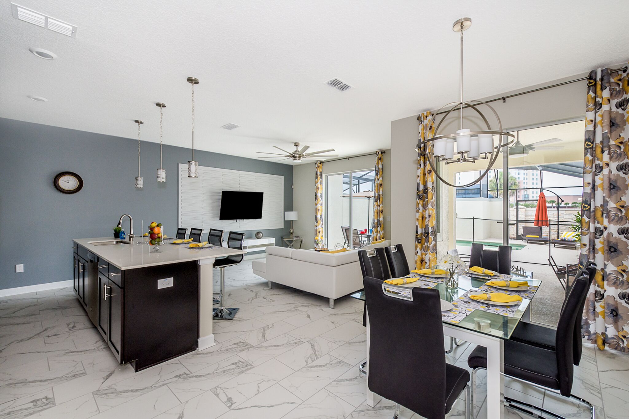 A modern kitchen with a central island, dining area with a glass table, and a living space with a sofa and TV.