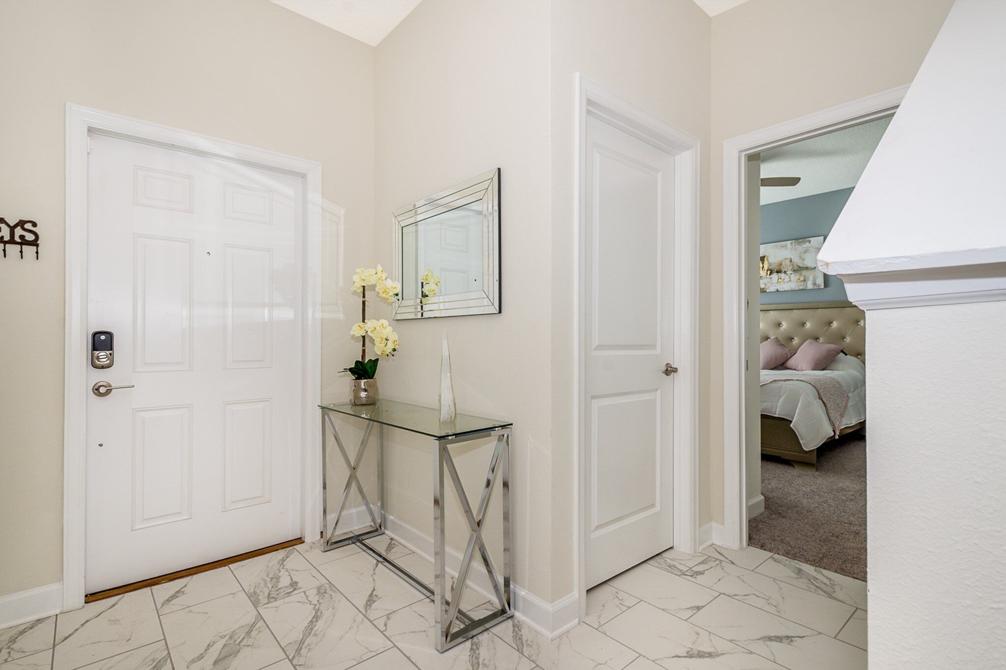 A hallway with a glass console table, a mirror, and a bed in the adjacent room.