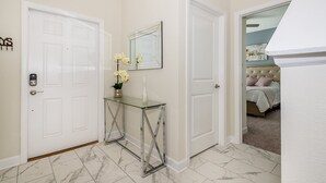 Un pasillo con una mesa consola de vidrio, un espejo y una cama en la habitación contigua.