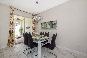 A dining area with a glass table, black chairs, a chandelier, and a large mirror on the wall.