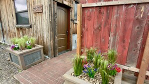 A rustic wooden building with a wooden door, a welcome sign, and two planter boxes with plants. - Bridger View - Studio (Gallatin County)