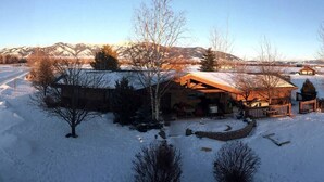 A snow-covered landscape with a wooden cabin featuring a porch and a fenced yard. - Bridger View - Studio (Gallatin County)