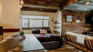 A cozy room with a wooden ceiling, a bed with a colorful quilt, a small table with a plant, and a bench. - Bridger View - Studio (Gallatin County)