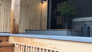 Una terraza de madera con barandilla, una planta en maceta y una puerta con panel de vidrio.