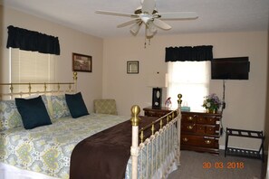 A bedroom with a bed, dresser, vanity, and a television.