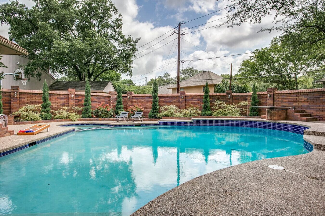 Una piscina rectangular con borde de azulejos, rodeada por un muro de ladrillo y follaje.
