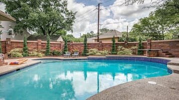 Una piscina rectangular con borde de azulejos, rodeada por un muro de ladrillo y follaje.