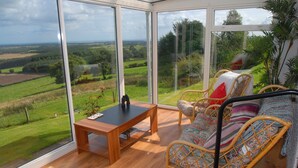 Un invernadero con suelo de madera, muebles de mimbre y vistas a un paisaje verde.