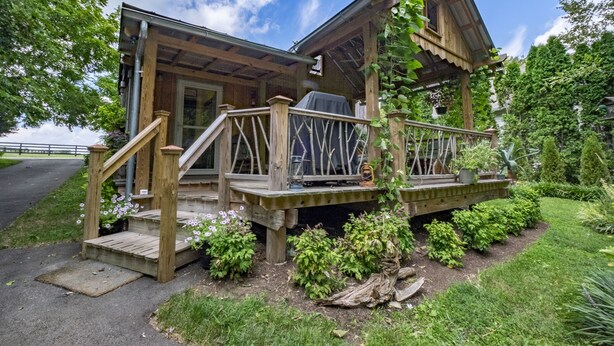 Una cabaña de madera con porche, zona de parilla cubierta y una pequeña terraza.