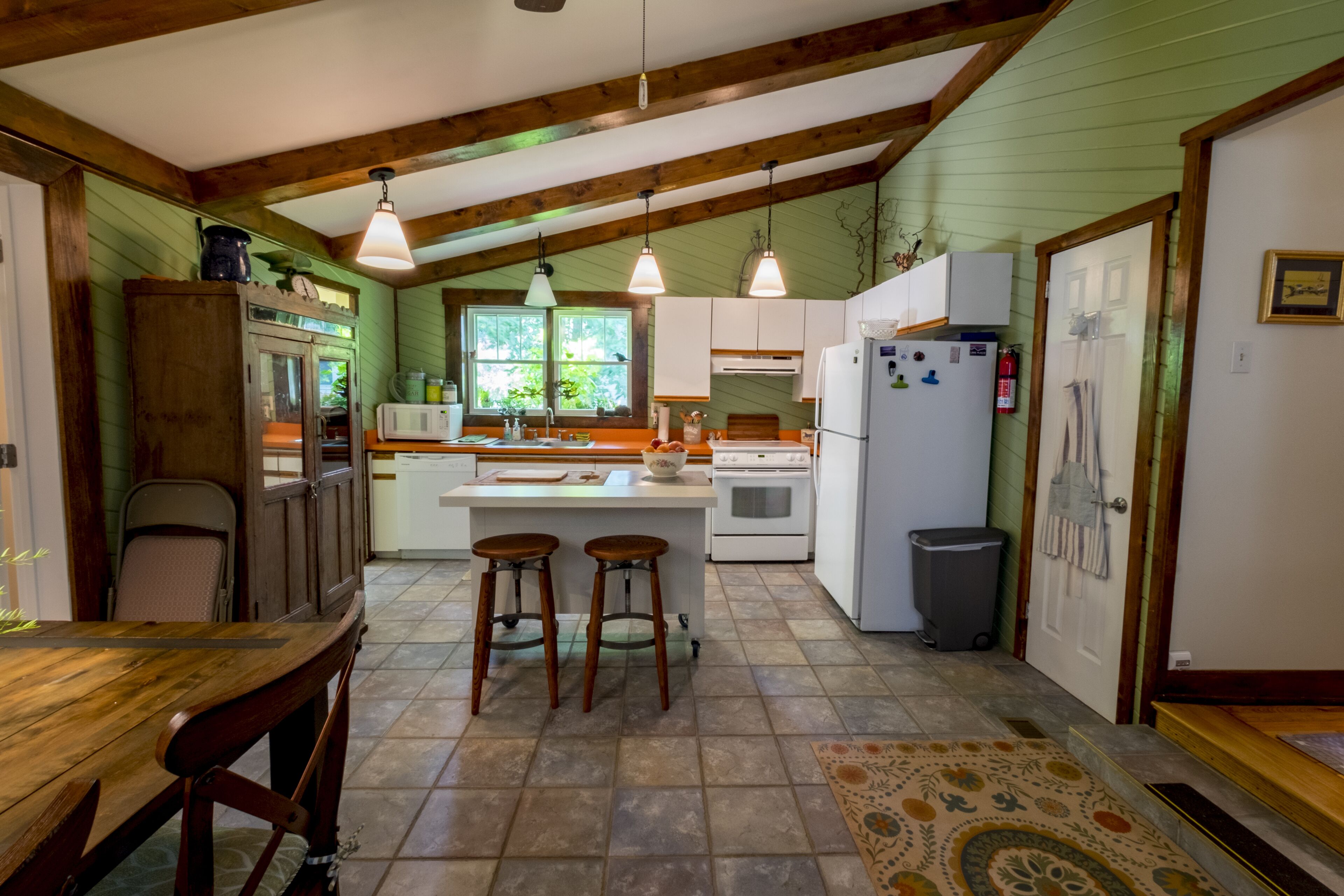 Une cuisine avec des poutres en bois, un îlot central doté de tabourets, un réfrigérateur et un four à micro-ondes.