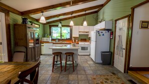 Una cocina con vigas de madera, una isla central con taburetes, un refrigerador y un microondas.