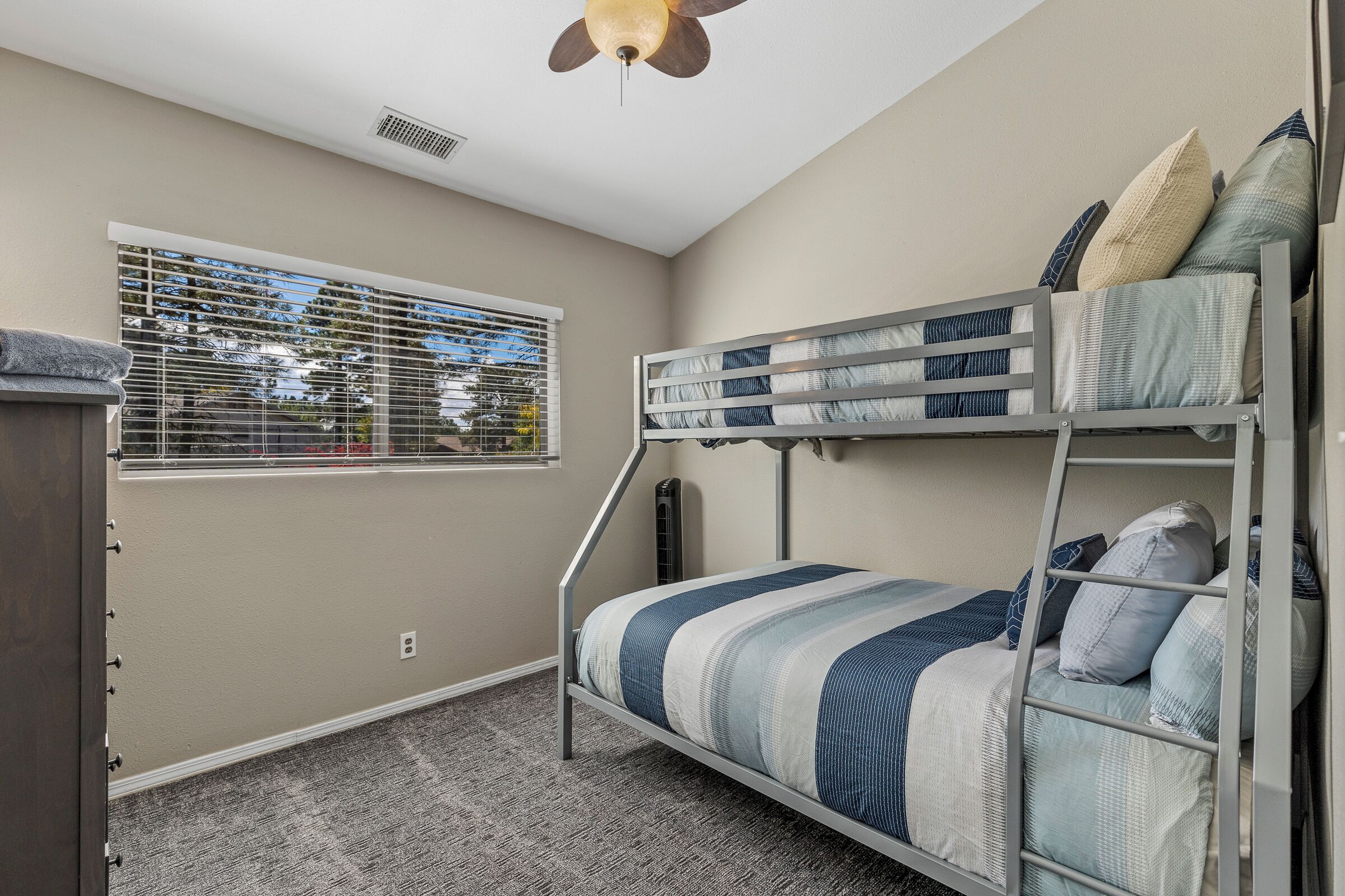 Un lit superposé avec une couvre-lit à rayures, une fenêtre avec des stores et un ventilateur de plafond.