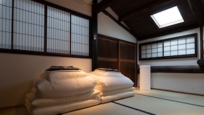 A traditional Japanese room with tatami flooring, a futon bed, sliding doors, and a skylight.
