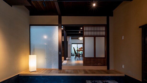 A traditional Japanese interior with a sliding door, a small table with chairs, and a bench with shoes.