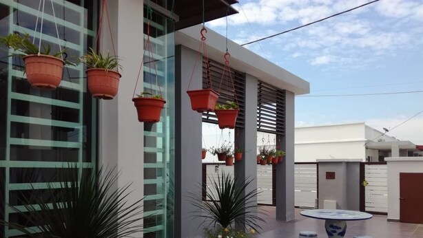 A modern building with hanging planters, a round table with blue and white ceramic stools, and potted plants on the ground. - KKP Homestay Alor Setar (Alor Setar)
