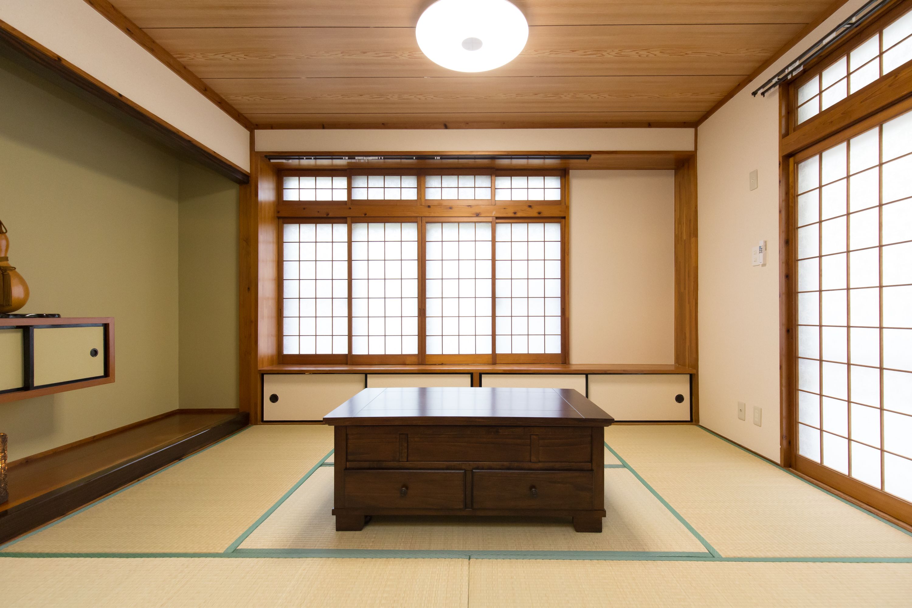 A traditional Japanese room with tatami flooring, a low wooden table, sliding shoji doors, and a ceiling light fixture.