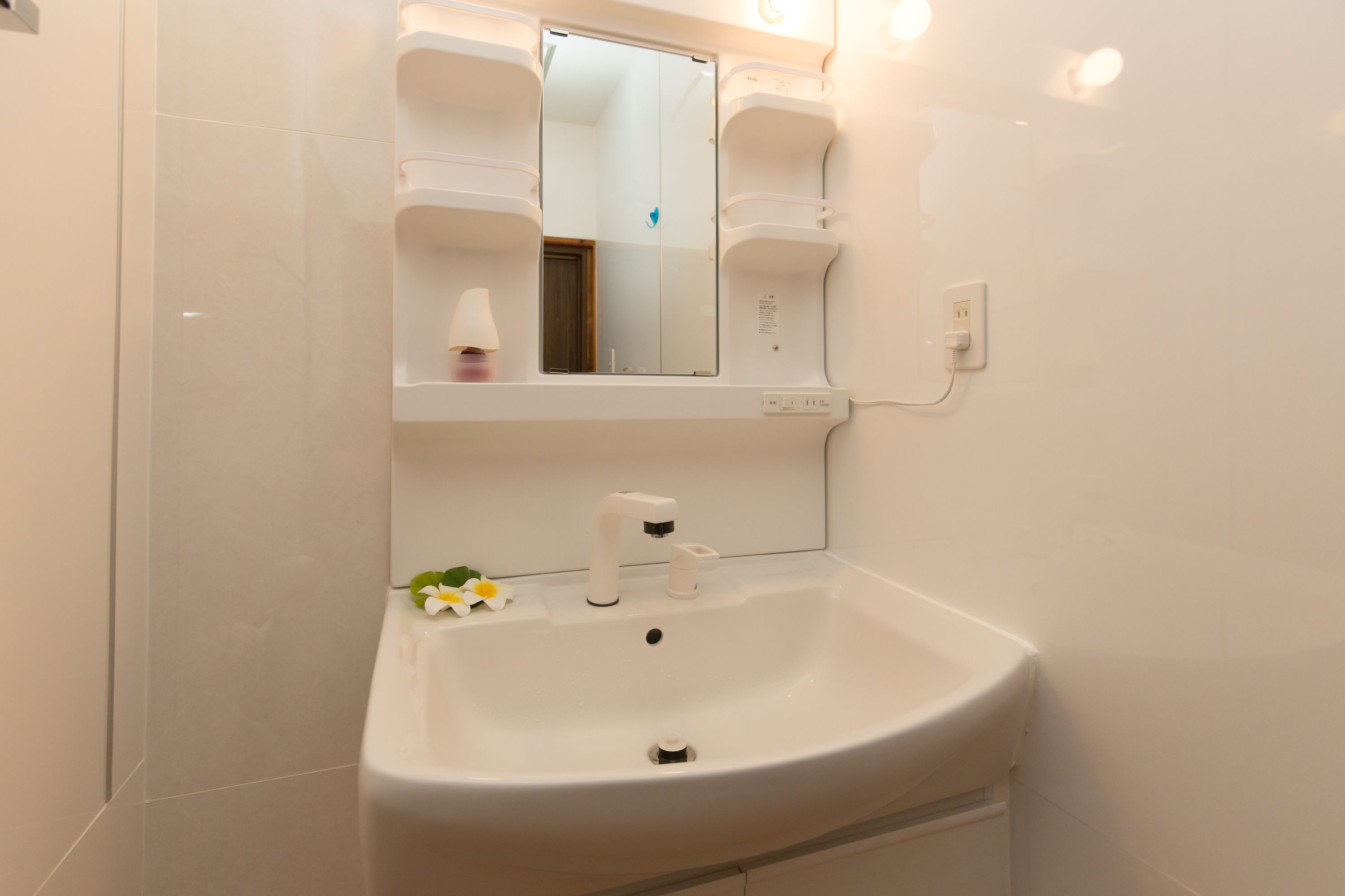 Une salle de bain avec un lavabo blanc, un miroir et un luminaire fixé au mur.