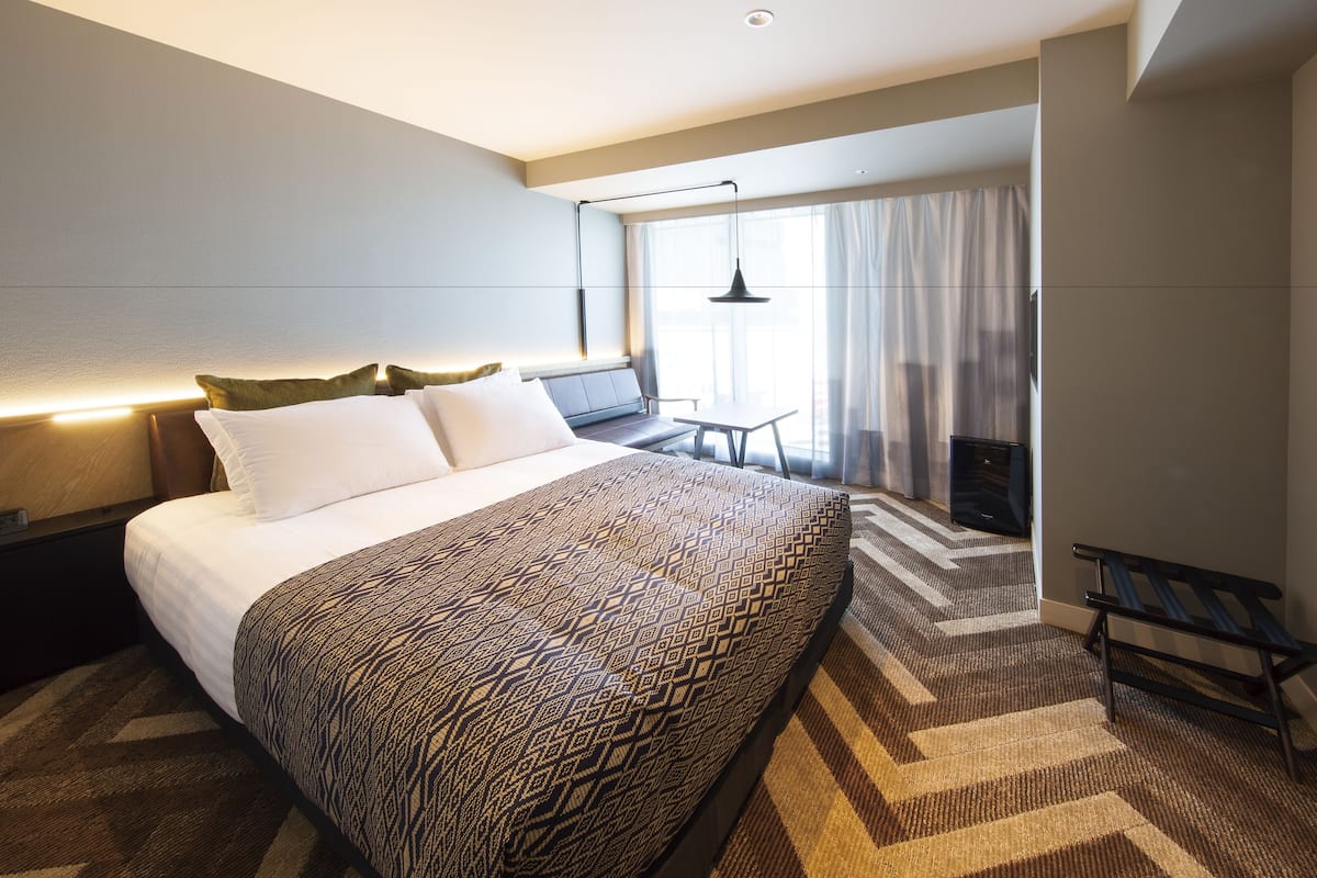 A hotel room with a large bed, a desk, and a bench.