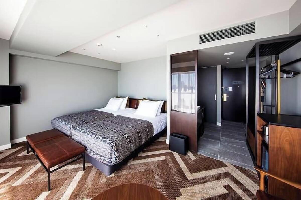 A modern hotel room with a large bed, a bench, a TV, and a walk-in closet.
