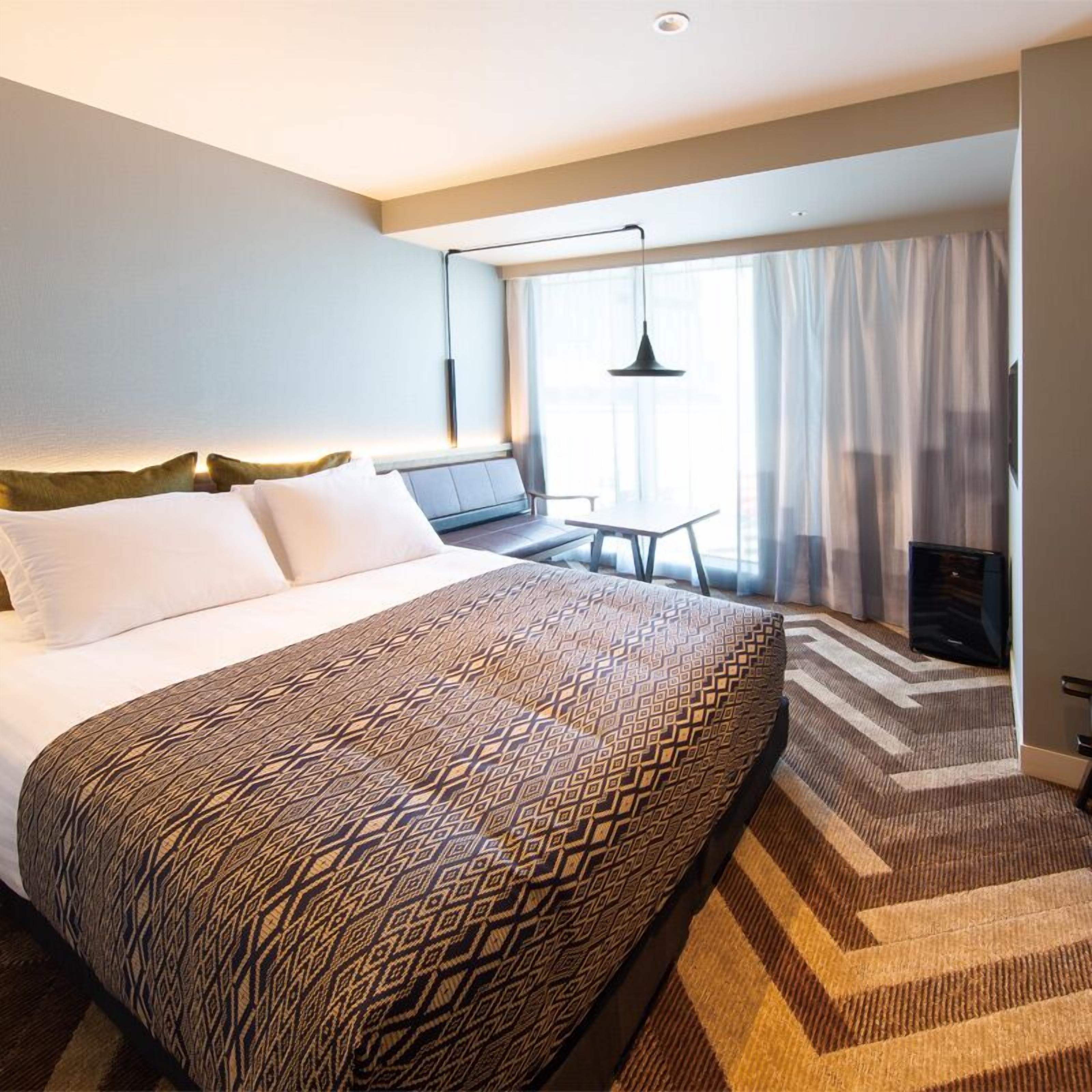 A hotel room with a large bed, a desk, a chair, and a TV.