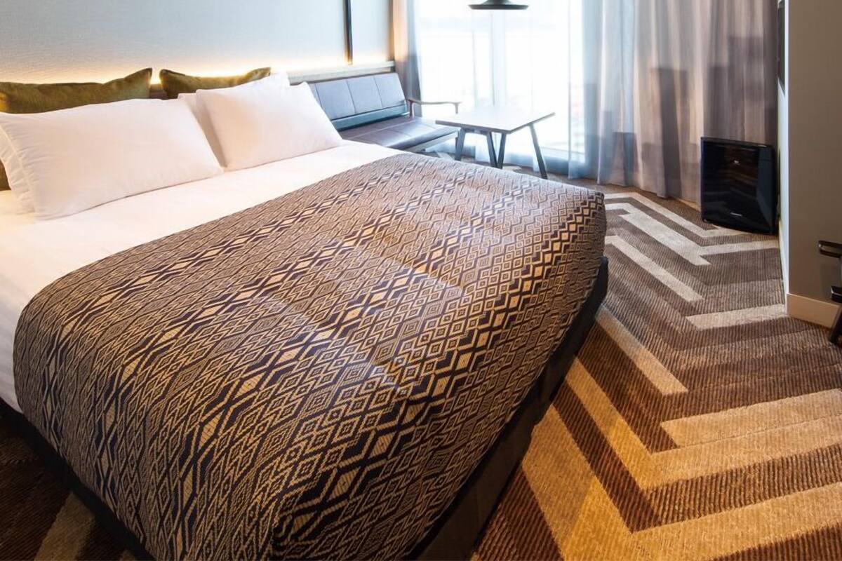 A hotel room with a large bed, a desk, a chair, and a TV.