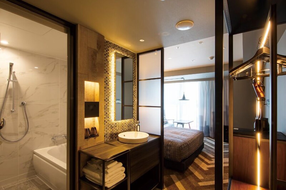 A modern bathroom with a bathtub, a sink, and a shower. There is a mirror above the sink and a window in the background.