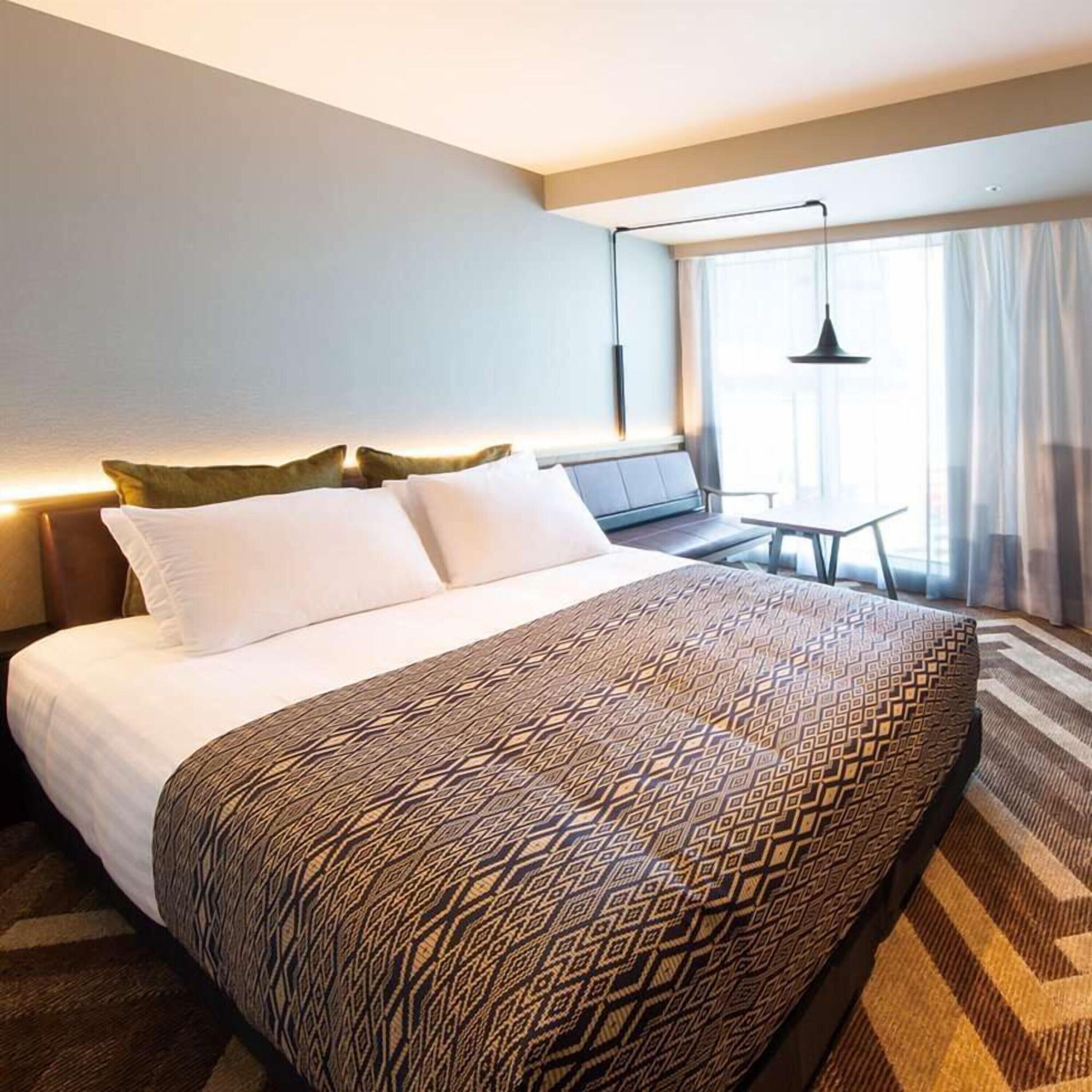 A hotel room with a large bed, a desk, and a window with curtains.