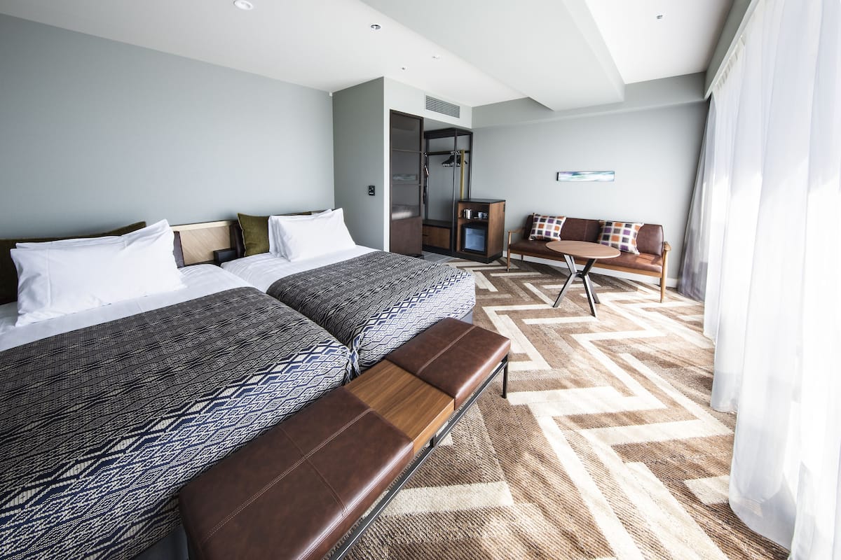 A hotel room with two beds, a bench, a sofa, a small table, and a wardrobe.