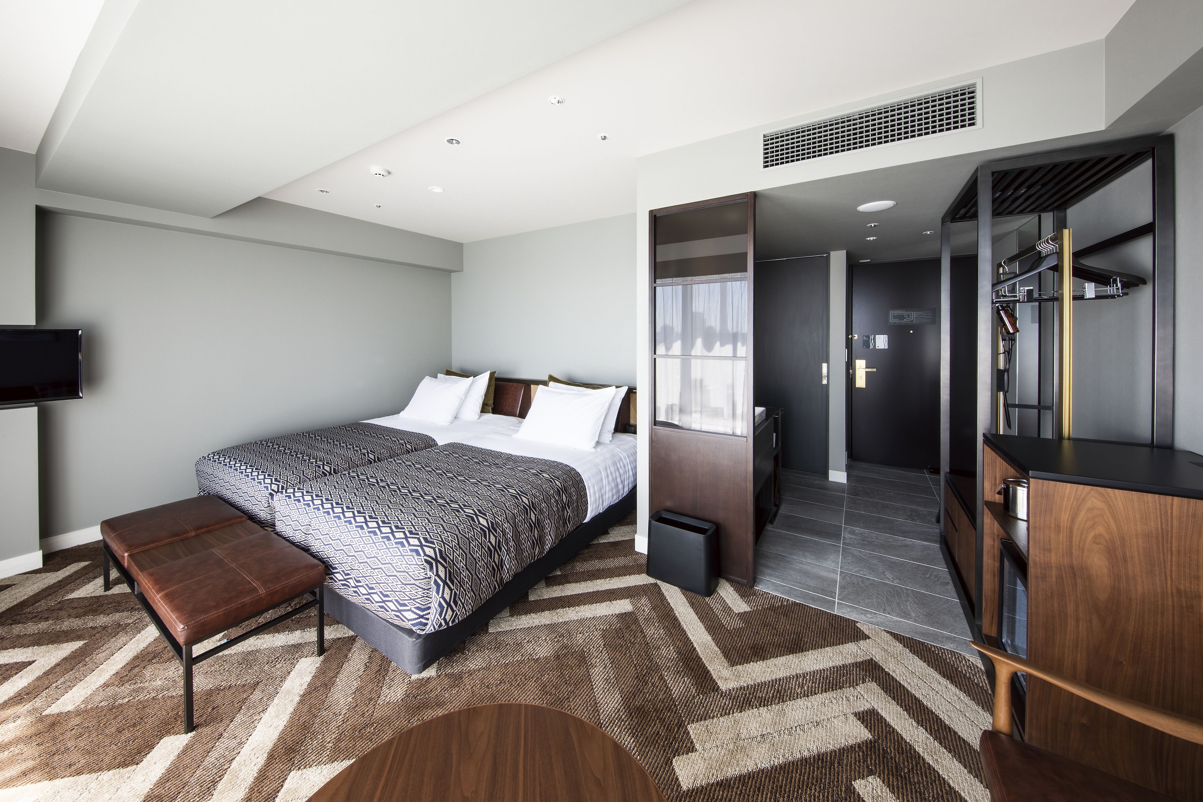 Un dormitorio moderno con una cama grande, un banco, un armario y un televisor en la pared.