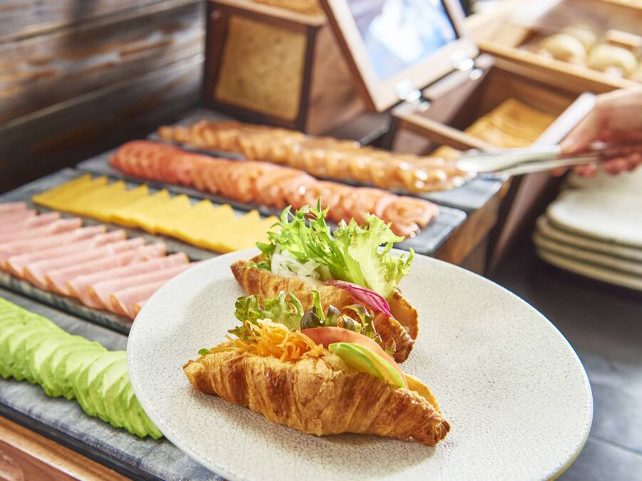 A buffet with various food items including sliced meats, cheeses, and a plate with a croissant and salad.