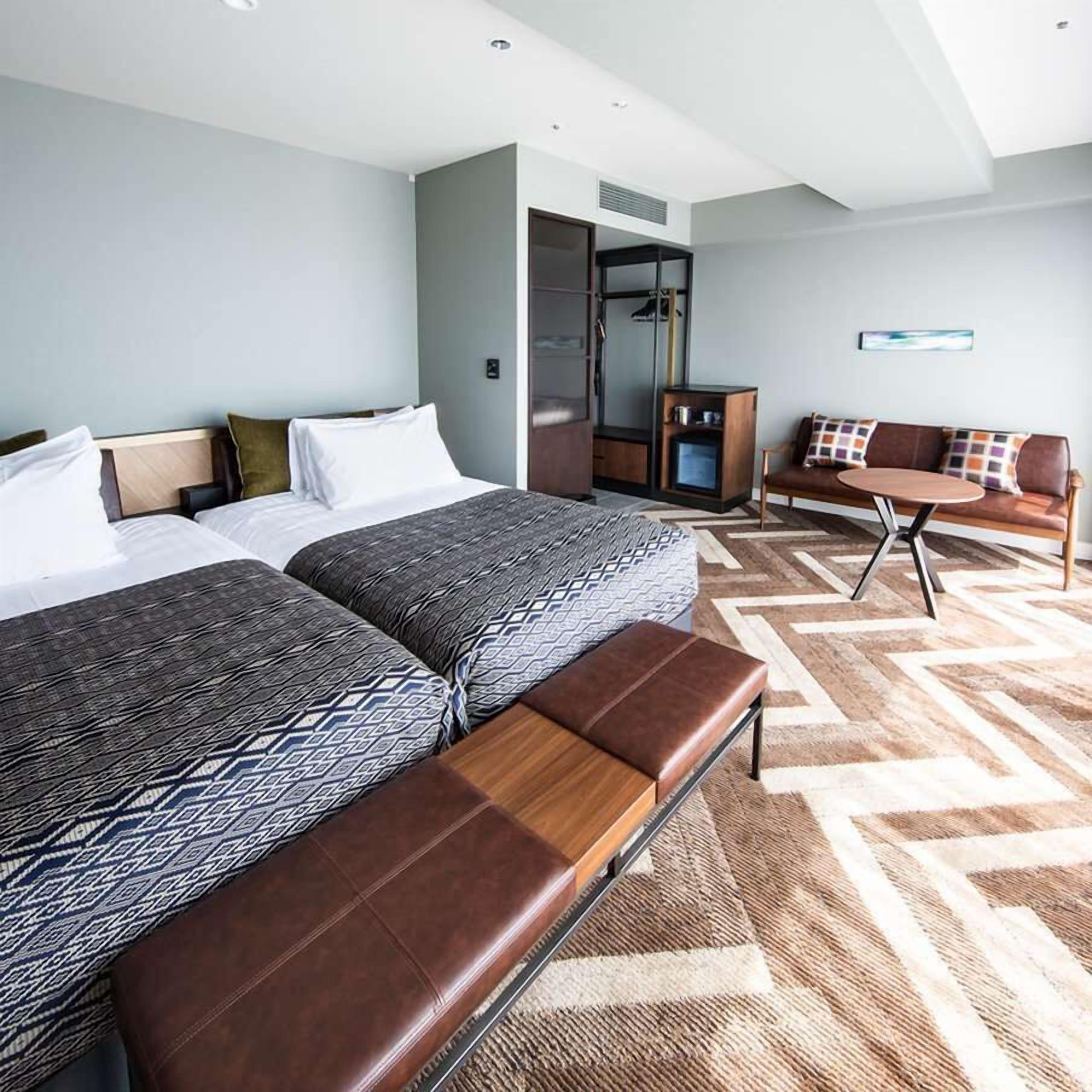 Une chambre d’hôtel avec deux lits, un canapé, une petite table et un banc.