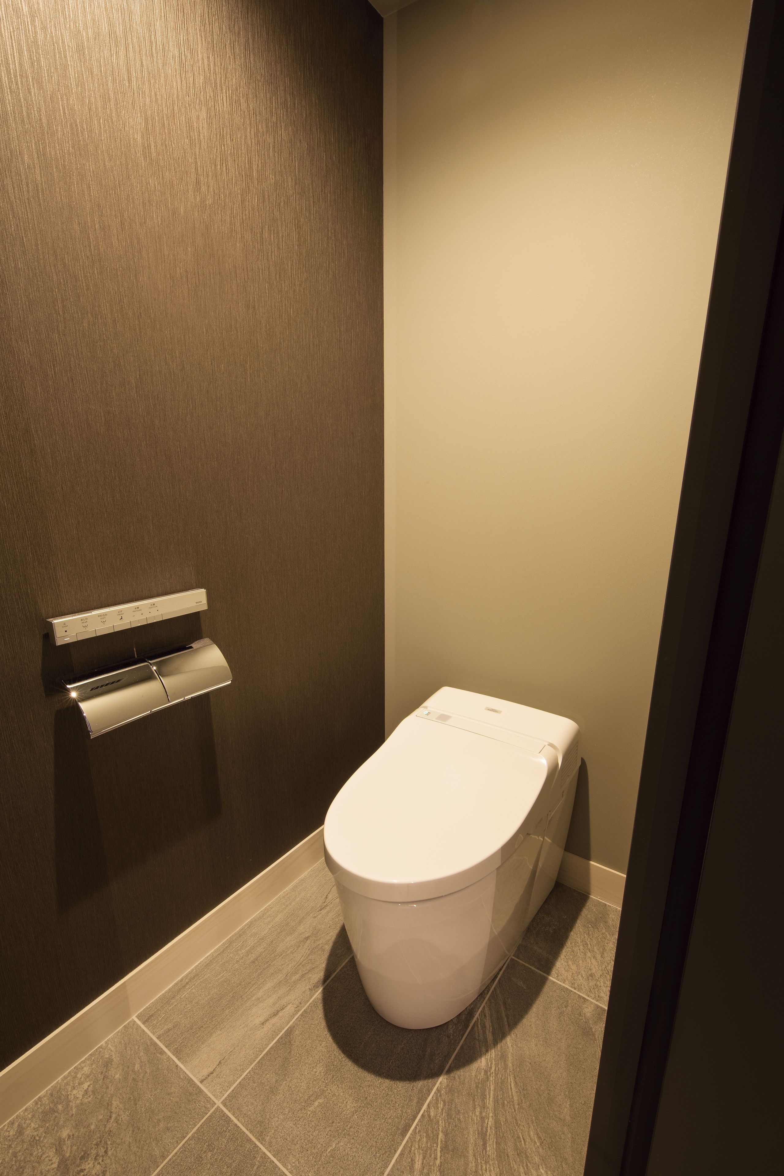 A modern bathroom with a toilet, a towel dispenser, and a wall-mounted soap dispenser.