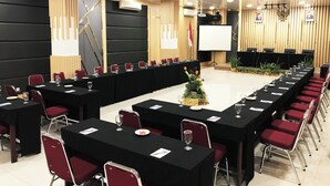 Un salón de conferencias con una larga mesa, sillas rojas y una pantalla para proyector.