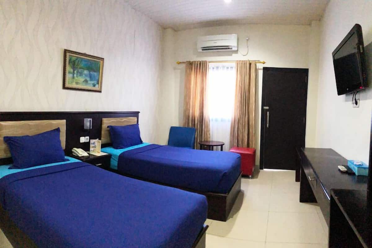 Habitación de hotel con dos camas, un escritorio, una silla, aire acondicionado, televisión y un cuadro en la pared.